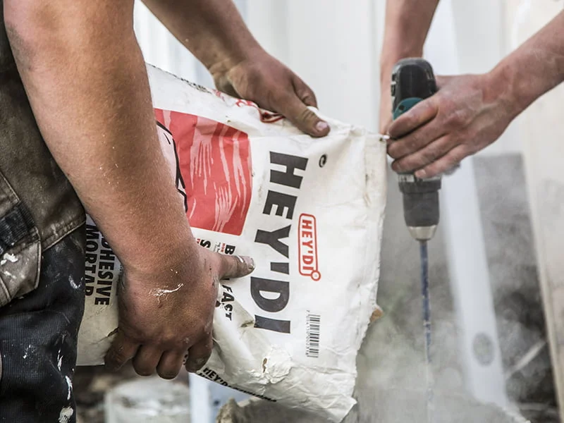 To personer blander byggemateriale med drill i støvete byggeområde.