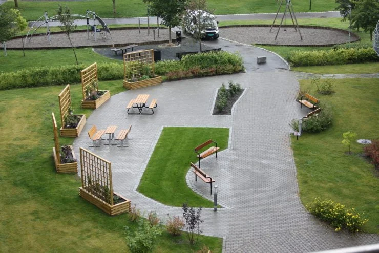 Moderne uteområde med benker, bord og trestativ omgitt av gress og gangsti