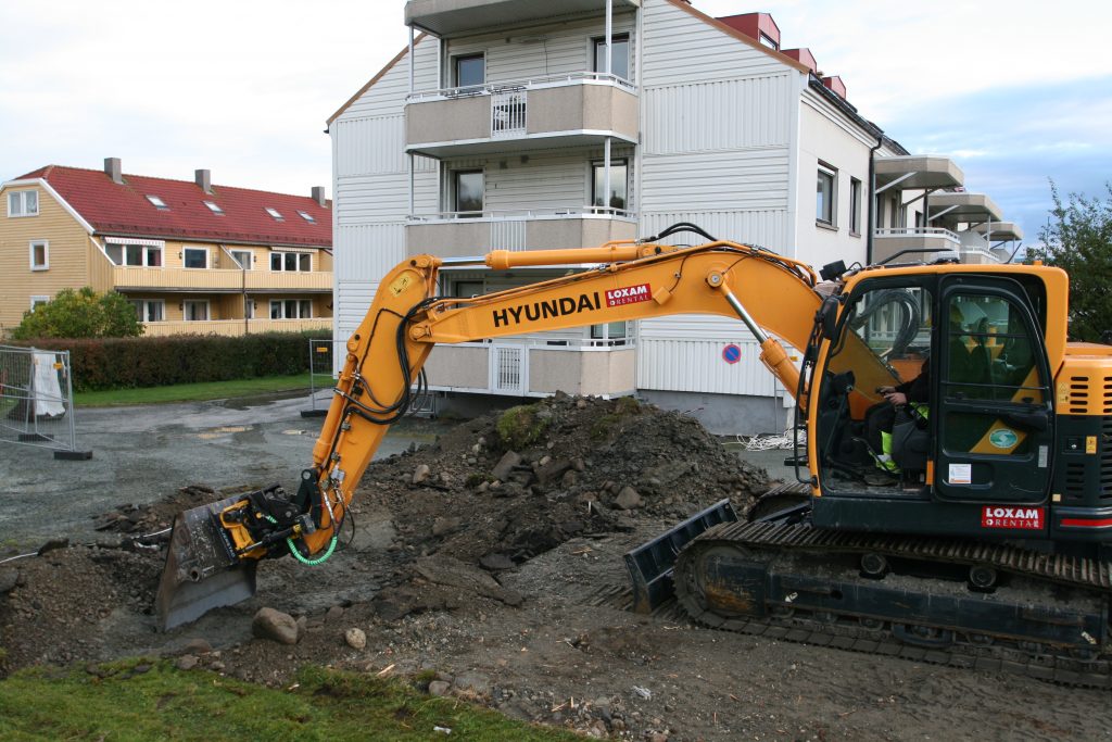 Gul gravemaskin fra Hyundai graver jord foran boligblokker