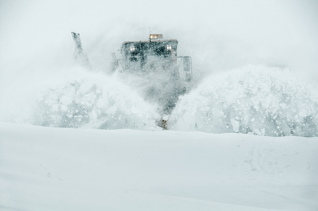 Stor snøplog rydder vei under kraftig snøfall med snø virvlende i luften