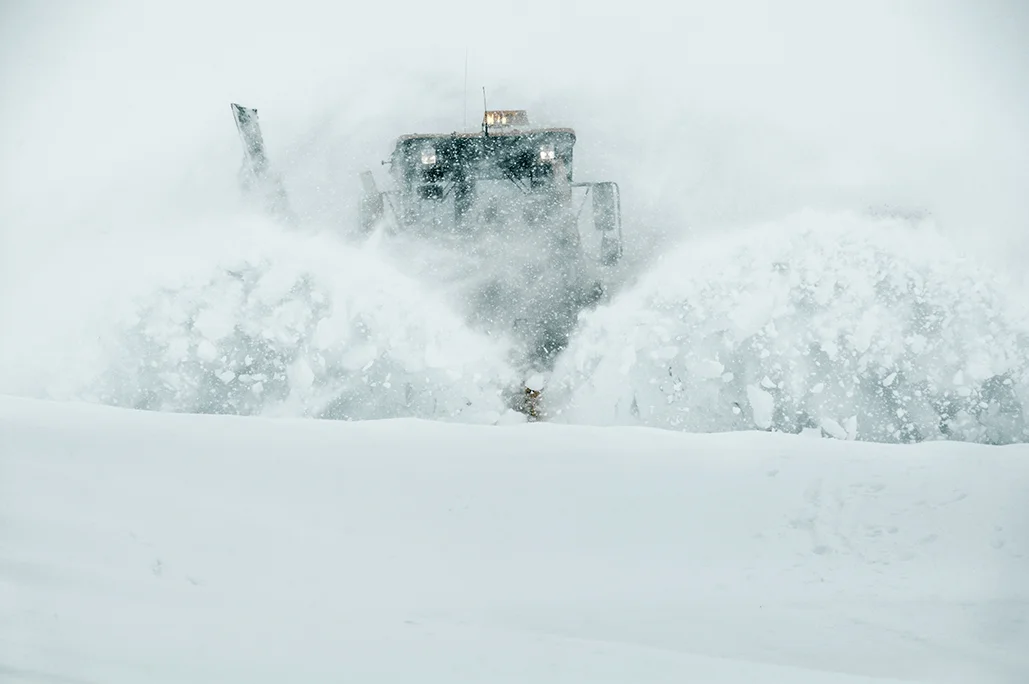 Stor snøplog rydder vei under kraftig snøfall med snø virvlende i luften