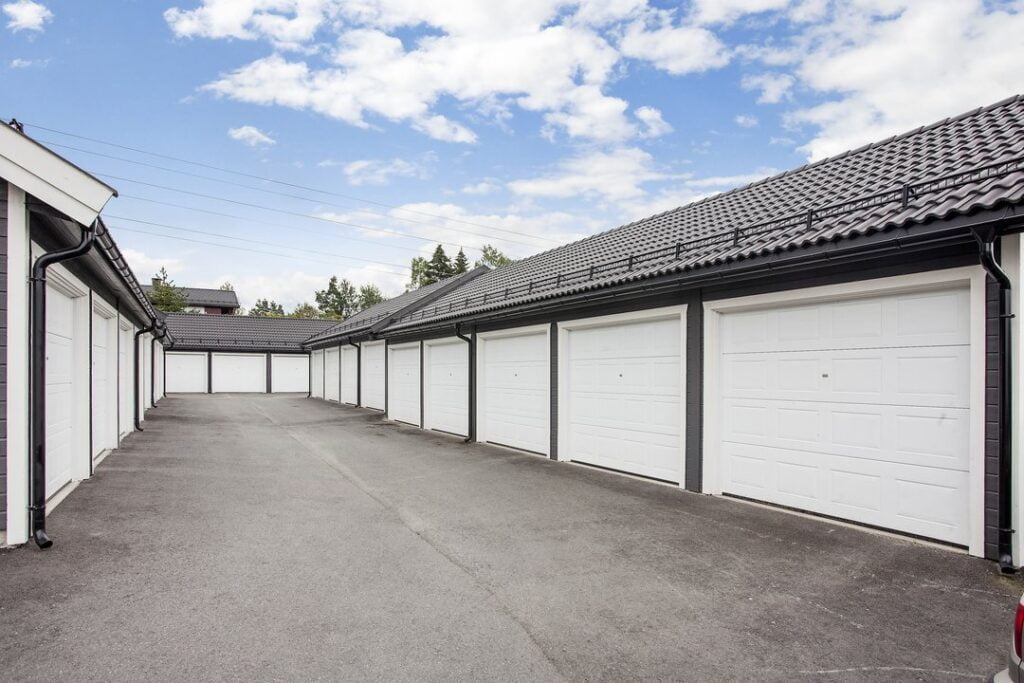 Rekke med garasjer med hvite porter og asfalt foran under blå himmel
