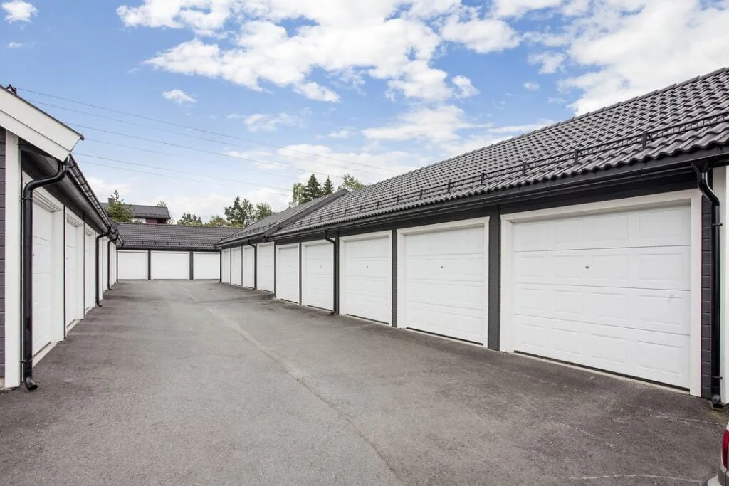 Rekke med garasjer med hvite porter og asfalt foran under blå himmel