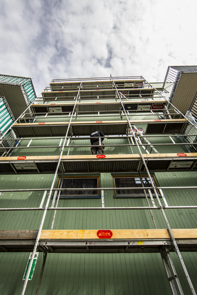Person står på stillas foran grønn bygning under renovering eller vedlikehold