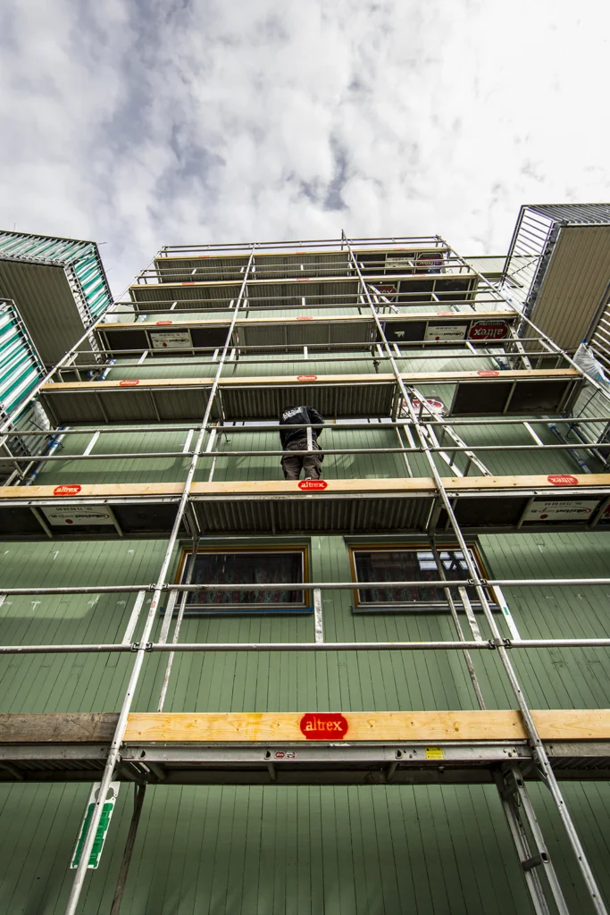 Person står på stillas foran grønn bygning under renovering eller vedlikehold