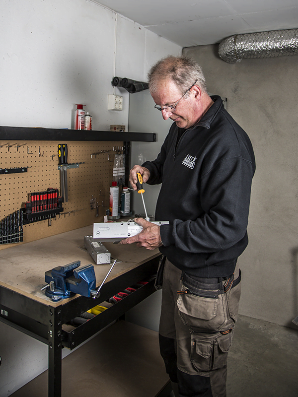 Person arbeider ved en arbeidsbenk med verktøy, monterer en metallkomponent med skrutrekker