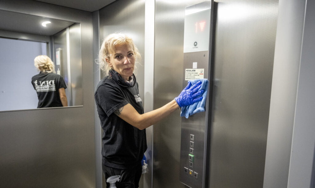 Person med blå hansker rengjør kontrollpanel i heis med klut