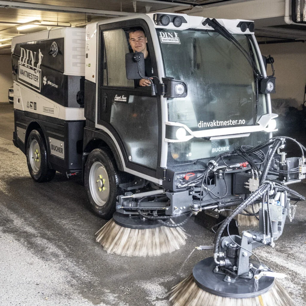 Kompakt feiemaskin med roterende børster rengjør gulv i parkeringsanlegg.