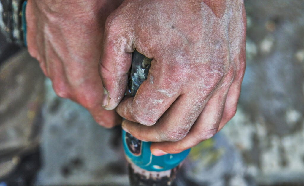 Nærbilde av hender som holder et verktøy med slitasje og støv