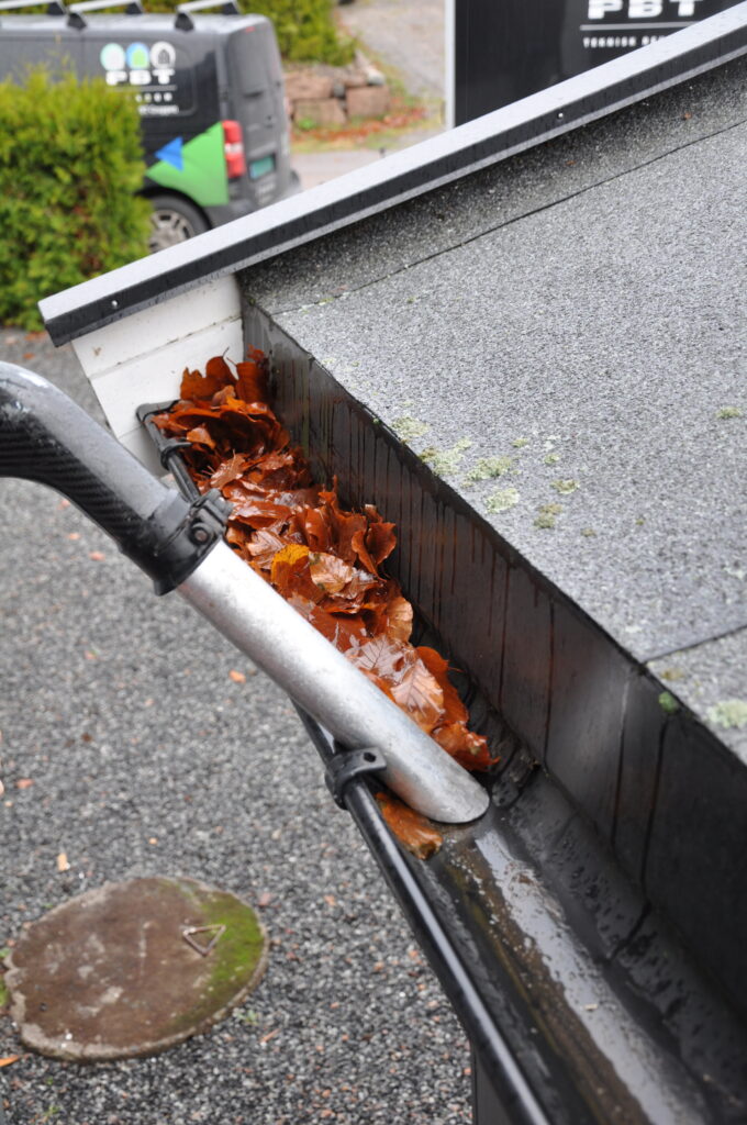 Støvsuging av takrenne fylt med våte høstblader