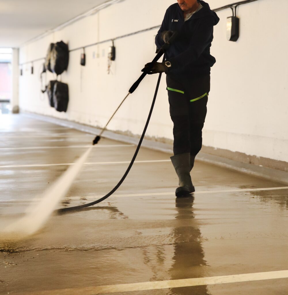 Person bruker høytrykkspyler på gulv i parkeringskjeller