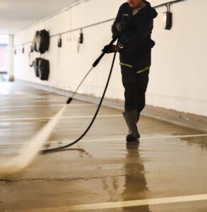 Person bruker høytrykkspyler på gulv i parkeringskjeller
