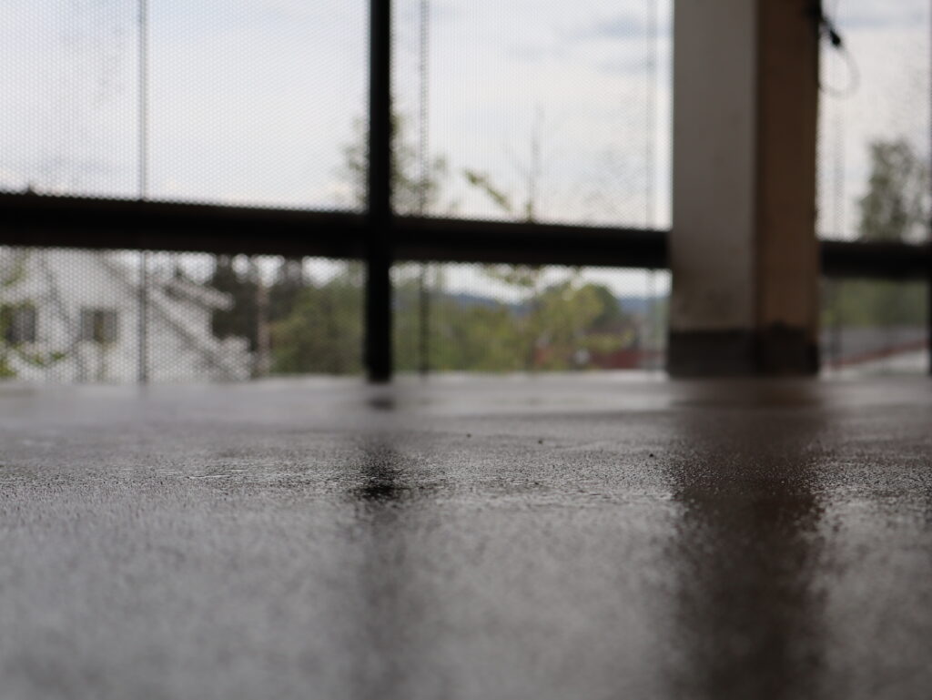 Nærbilde av vått betonggulv i parkeringshus med lysinnslipp