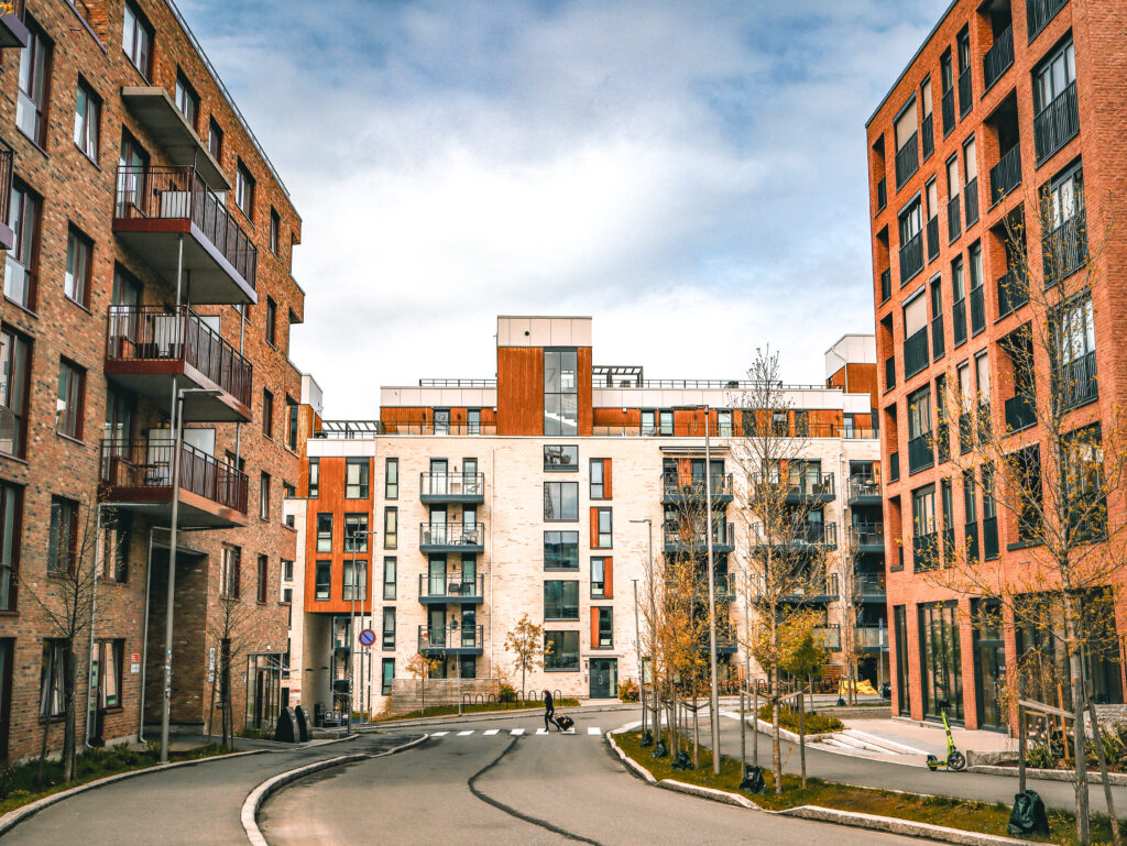 Moderne leilighetsbygg i murstein og betong med balkonger, trær og gangvei i et urbant boligområde.