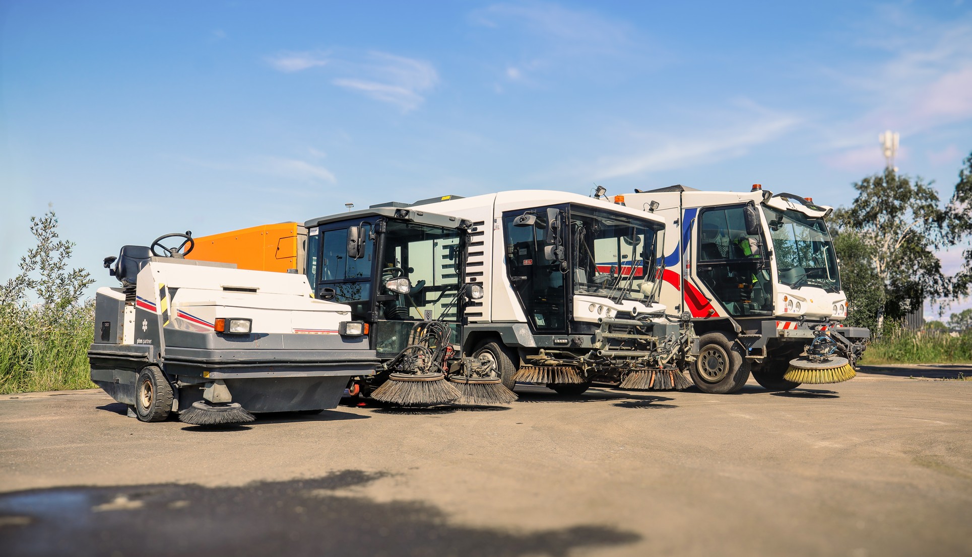 Tre feiemaskiner parkert på asfalt under blå himmel